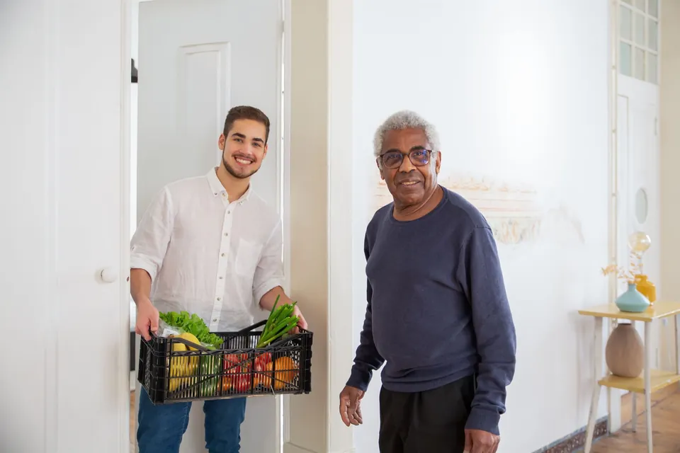 Un voluntario entrega una caja de verduras a un hombre mayor en su puerta