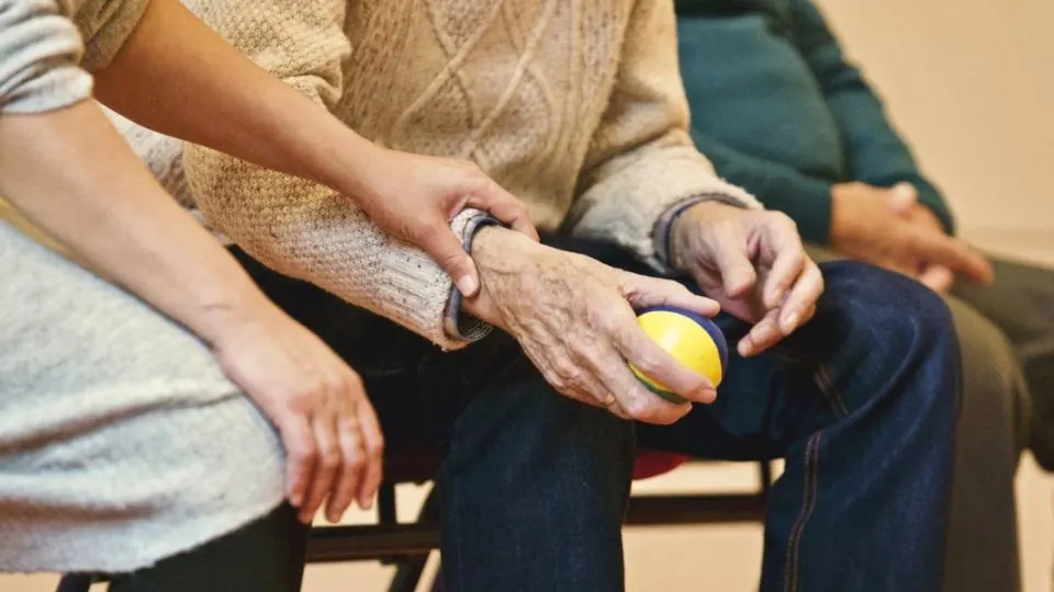 Una cuidadora acompaña a un hombre mayor en un ejercicio de rehabilitación